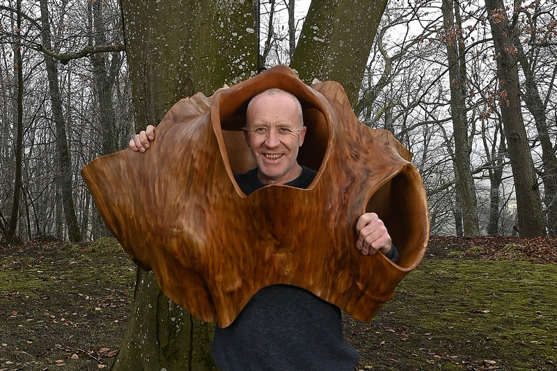 Künstler Bernhard Schmid mit einer Holzskulptur im Wald